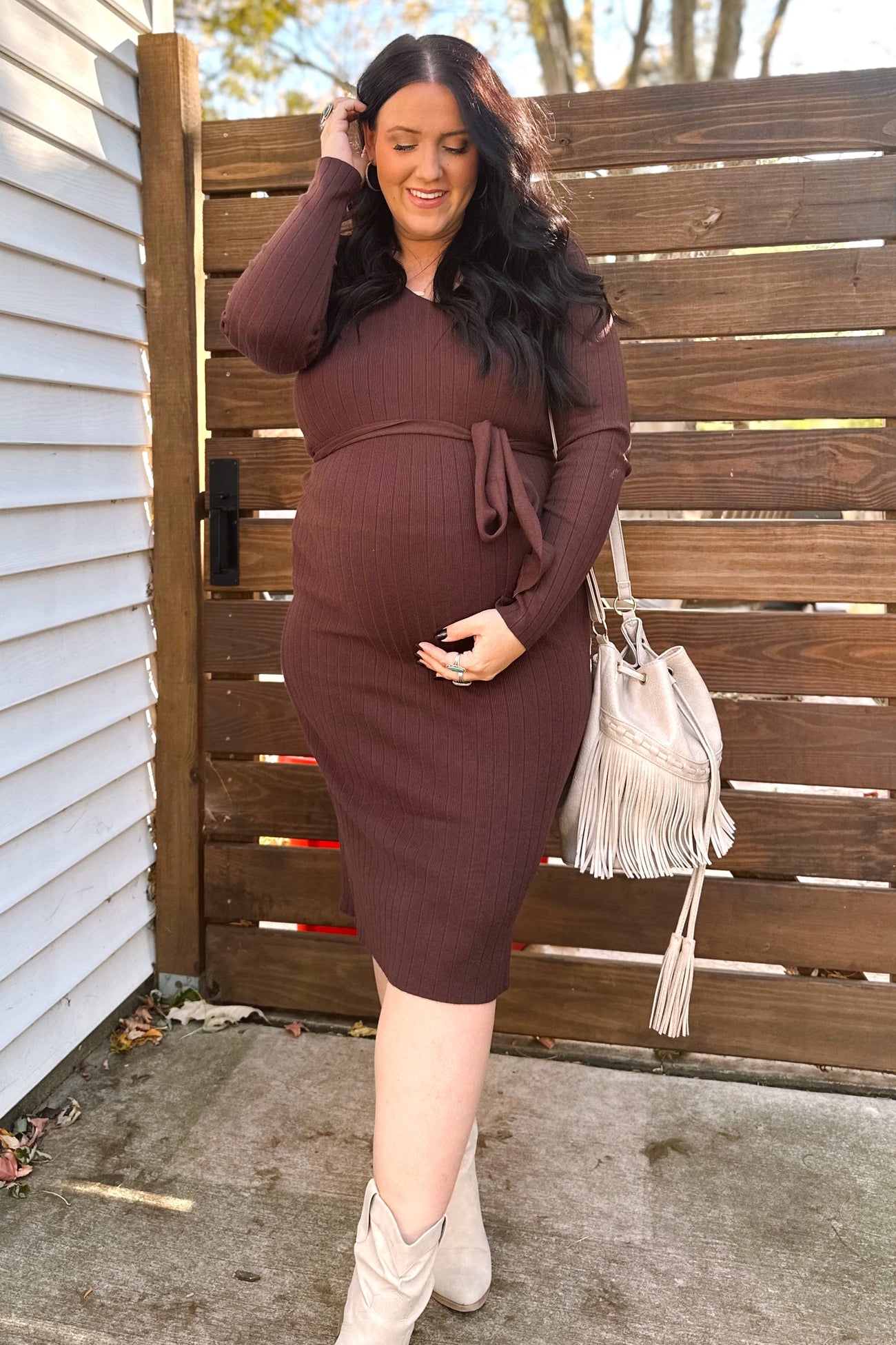 woman wearing a brown ribbed maternity dress with a tie waist and holding her baby bump outside