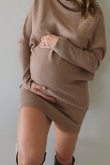 woman wearing a taupe long sleeve maternity sweater dress and holding her baby bump