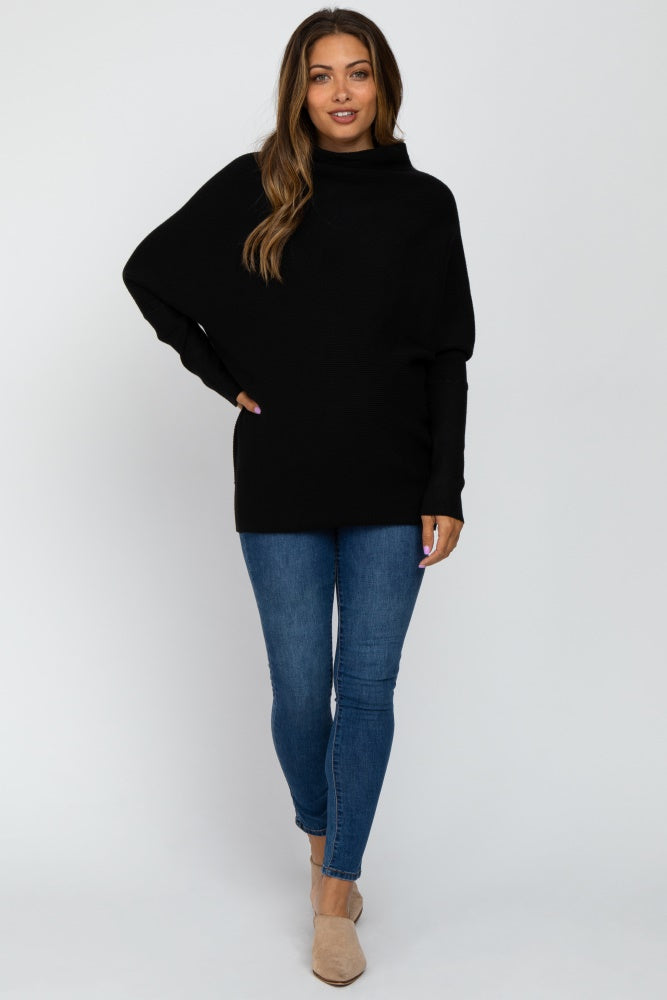 woman wearing a black oversized maternity sweater with a cowl neck and blue skinny jeans