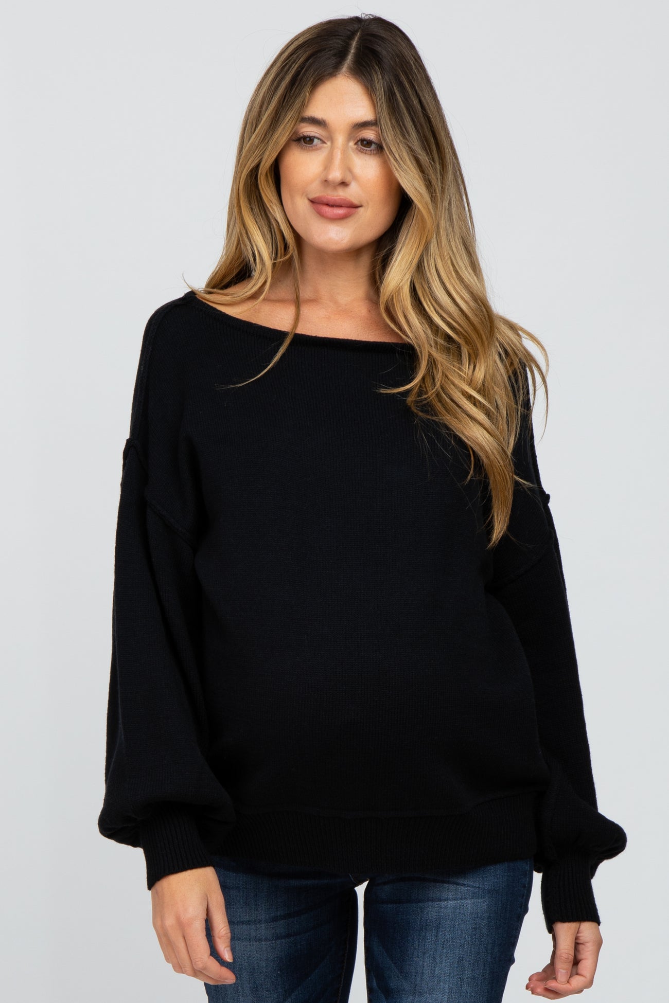 woman wearing a black off-the-shoulder maternity sweater with long sleeves and a relaxed fit, showcasing her baby bump