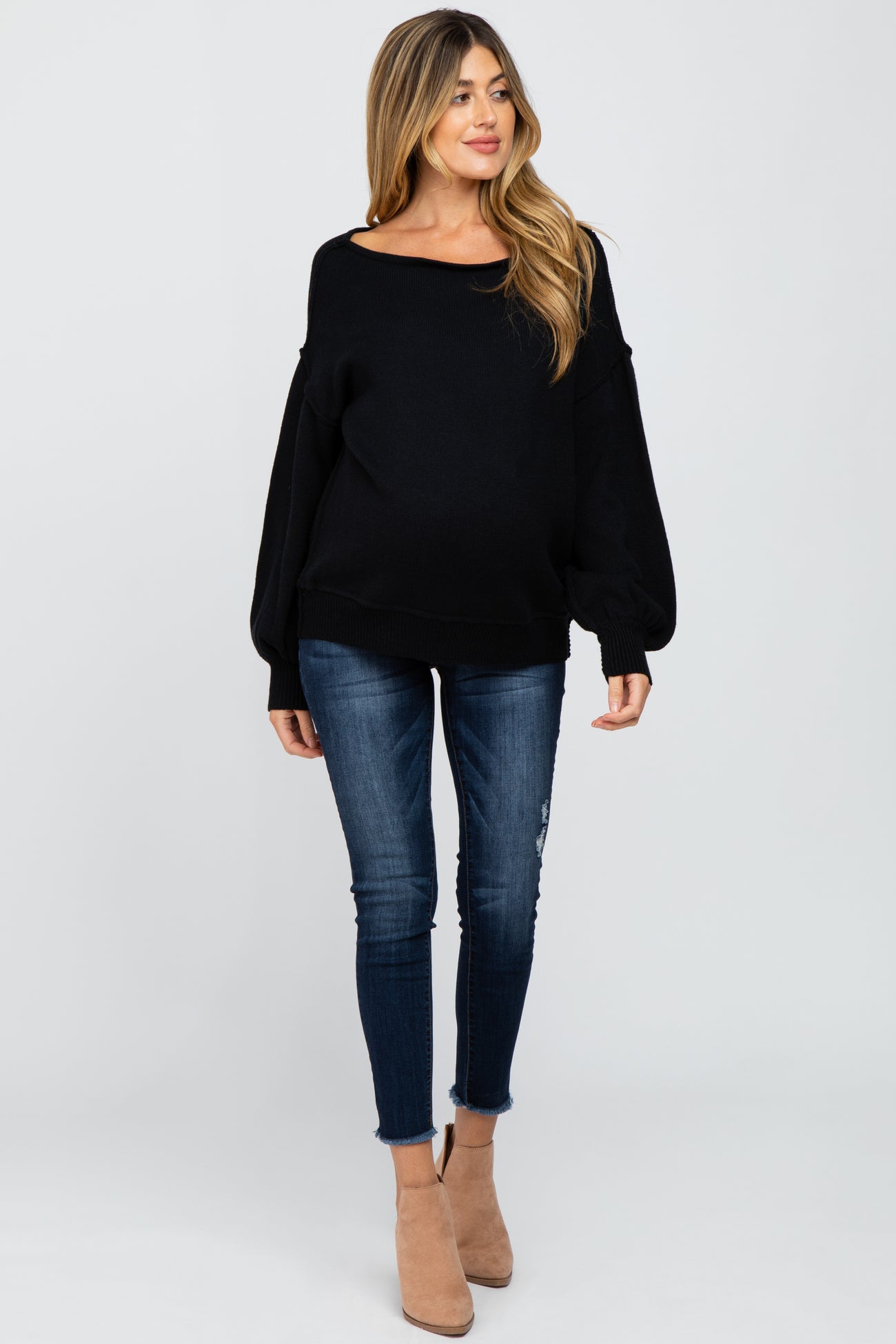 woman wearing a black oversized maternity sweater and distressed skinny jeans, with a visible baby bump