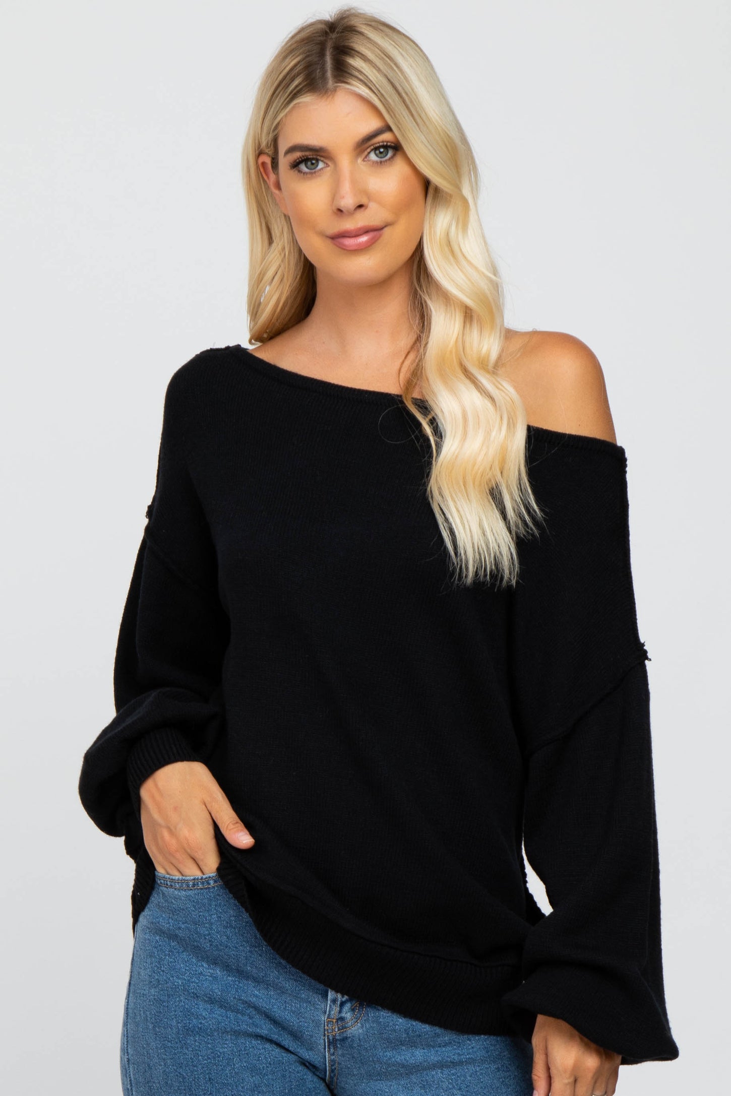 blonde woman wearing a black off-the-shoulder knit sweater and blue jeans
