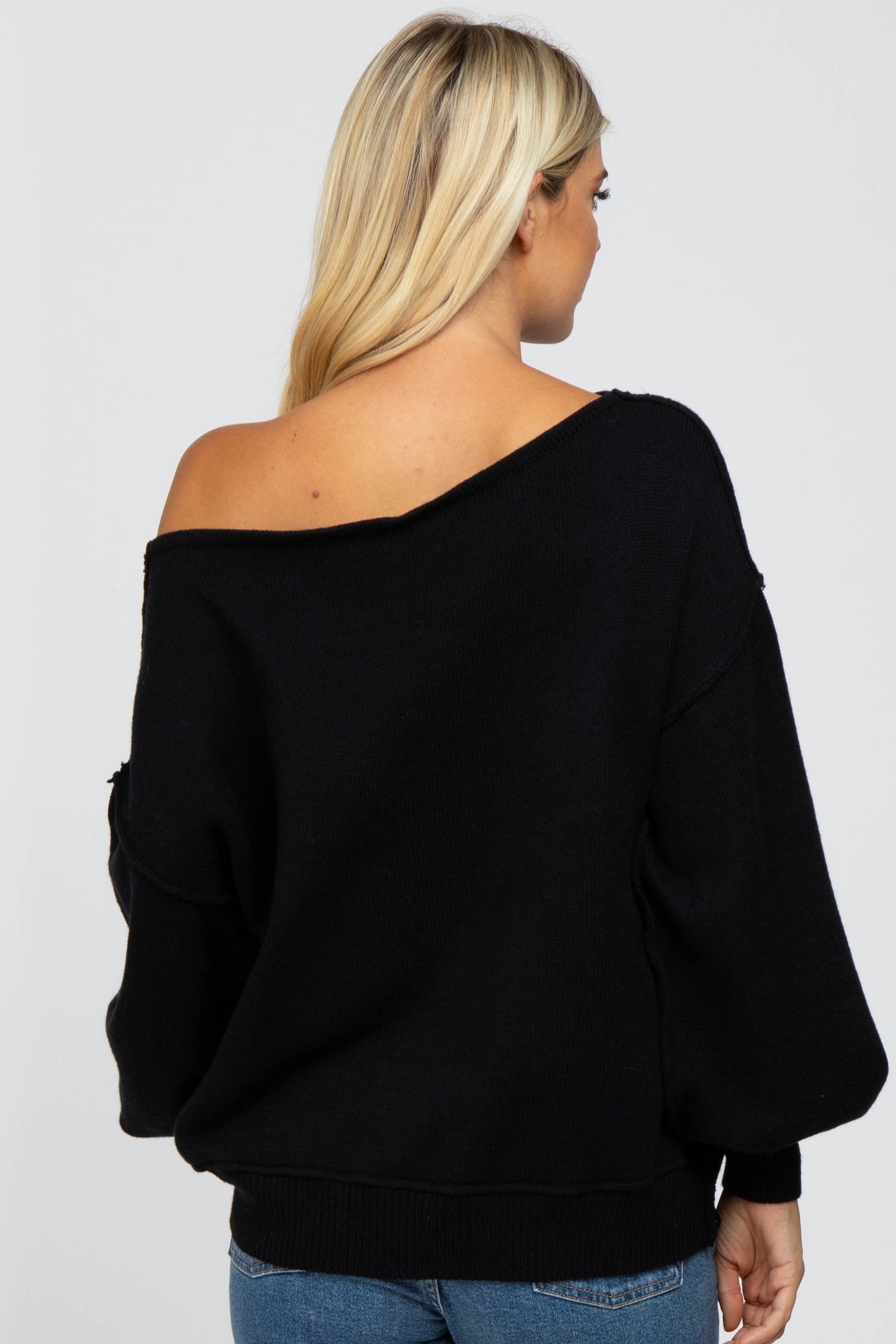 woman wearing a black off-shoulder sweater with balloon sleeves and a relaxed fit, shown from the back