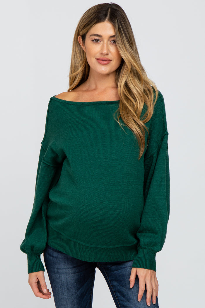 woman wearing a dark green off-the-shoulder maternity sweater and showing her baby bump