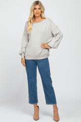woman wearing a light grey oversized sweater with a wide neckline, paired with blue cropped jeans and beige ankle boots