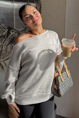 woman wearing a light gray off-shoulder sweater with rolled sleeves, holding an iced coffee and a designer handbag