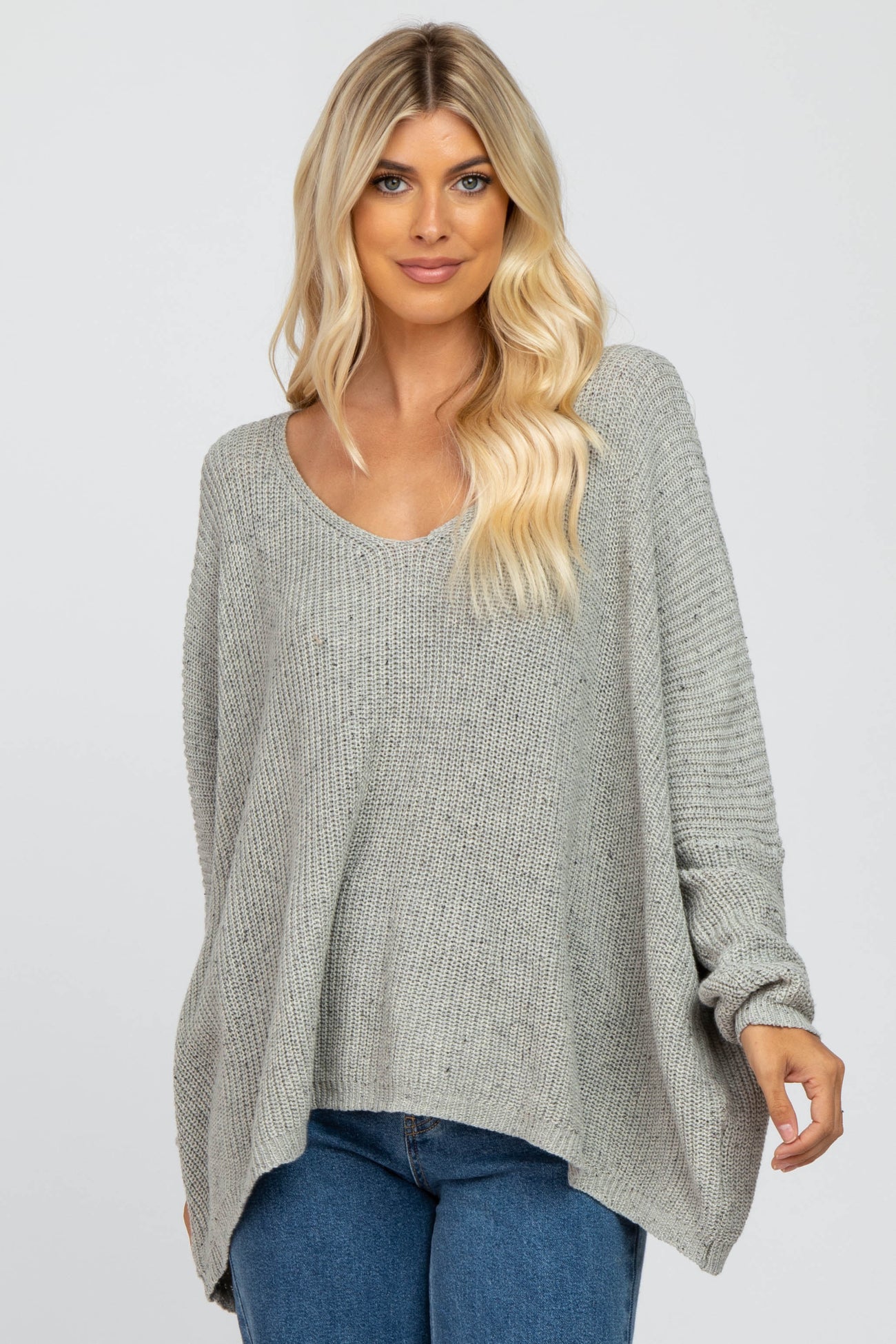 woman wearing a light gray oversized knit sweater with a scoop neckline and long sleeves, paired with blue jeans