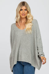 woman wearing a light gray oversized knit sweater with a scoop neckline and long sleeves, paired with blue jeans