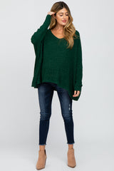 woman wearing a green maternity sweater with a v-neck and relaxed fit paired with dark jeans and ankle boots