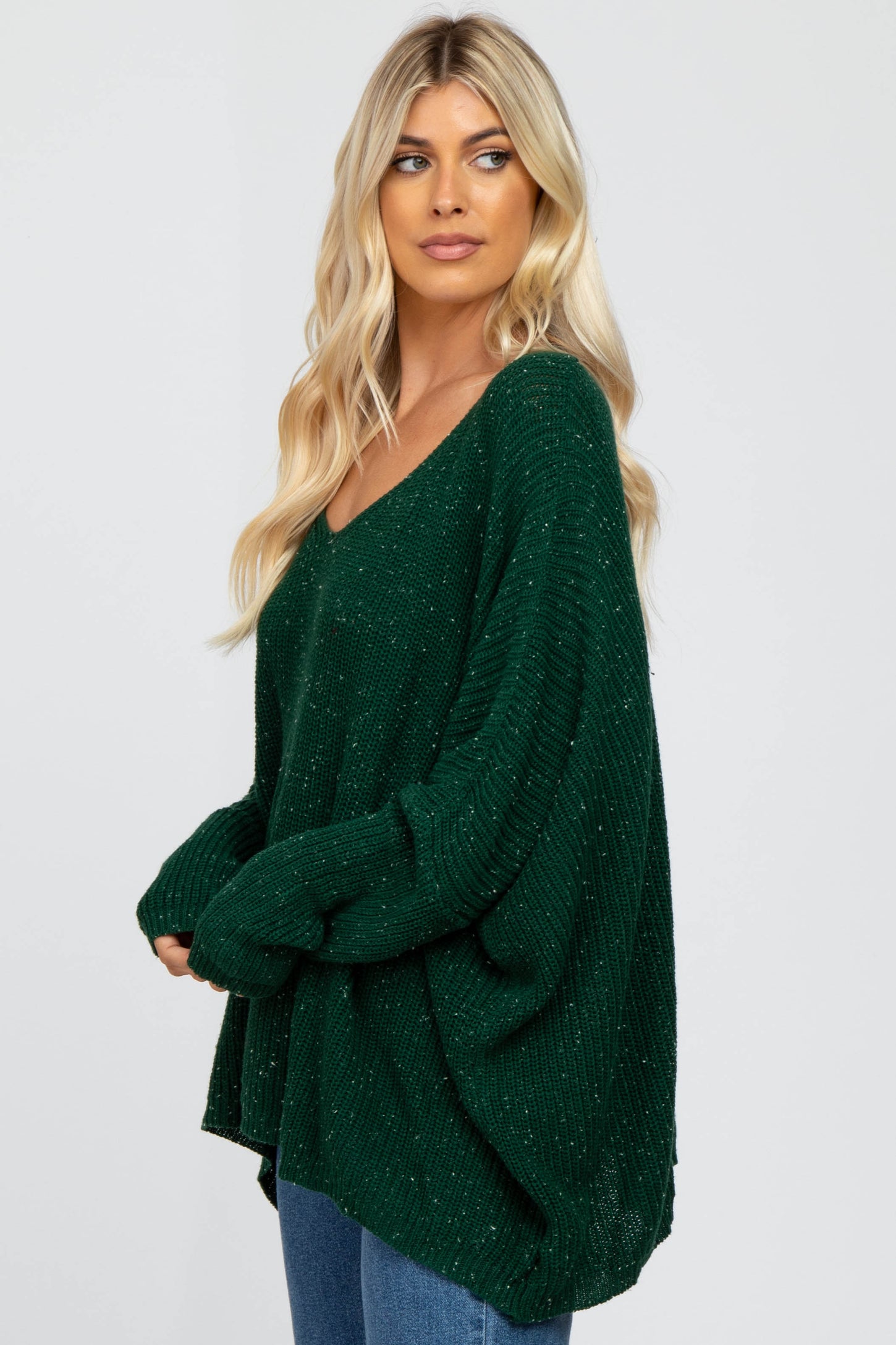 woman wearing a green oversized v-neck sweater with textured details and loose sleeves, styled with blue jeans