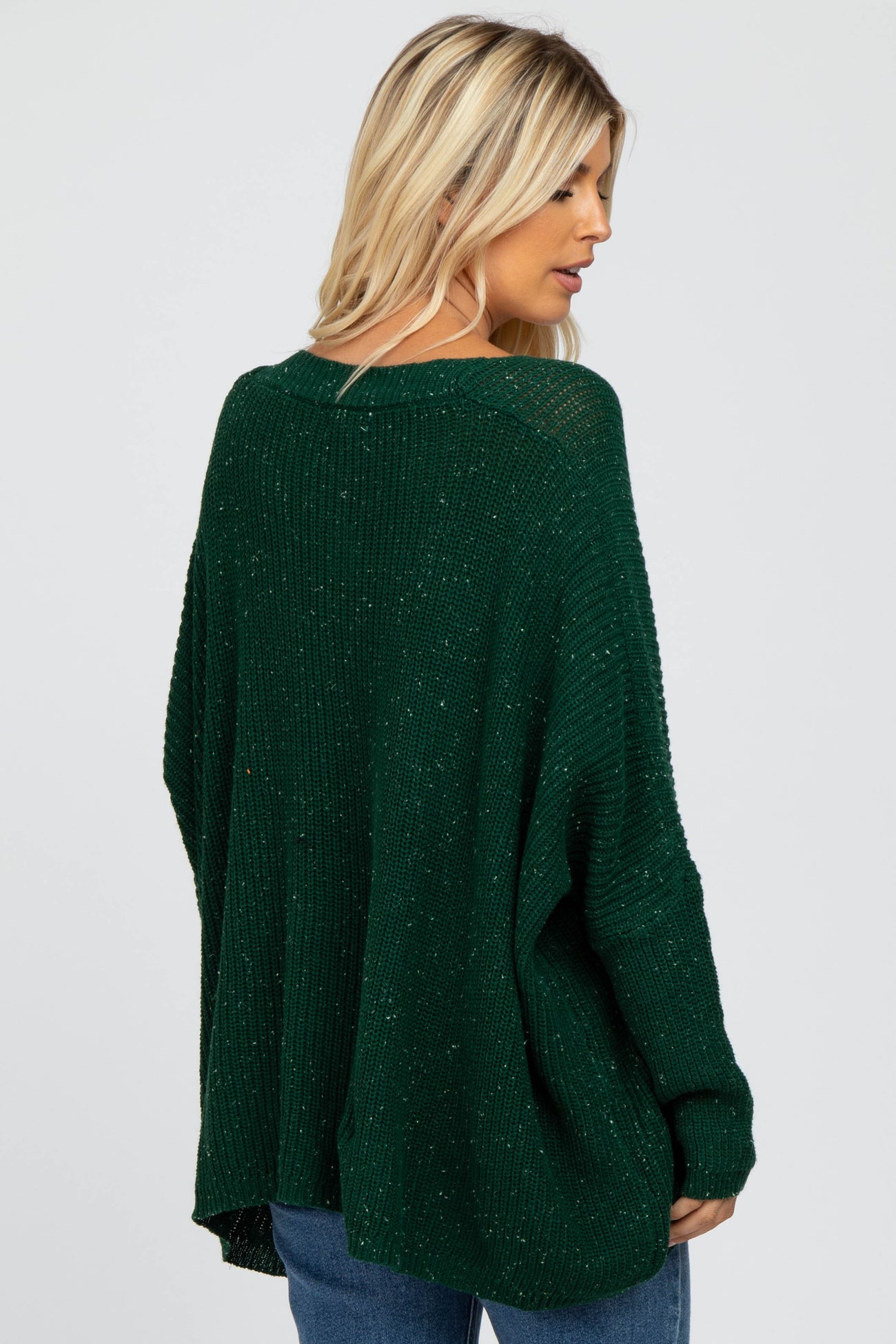 woman wearing a dark green oversized knit sweater with a relaxed fit and back detail, styled with blue jeans