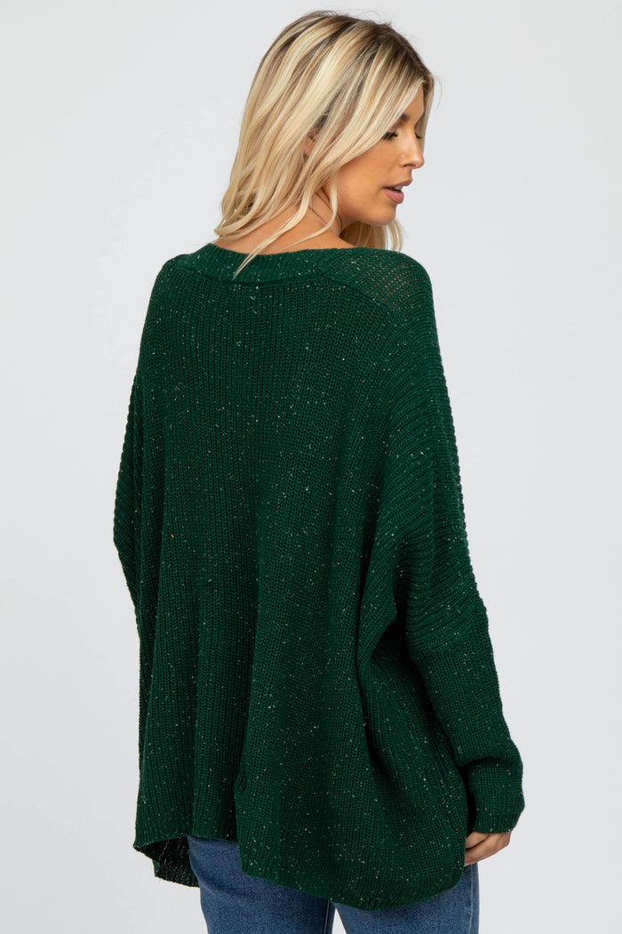 woman wearing a dark green oversized knit sweater with a relaxed fit and back detail, styled with blue jeans