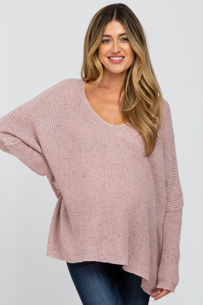 woman wearing a light pink oversized maternity sweater with a scoop neck and long sleeves, showing her baby bump