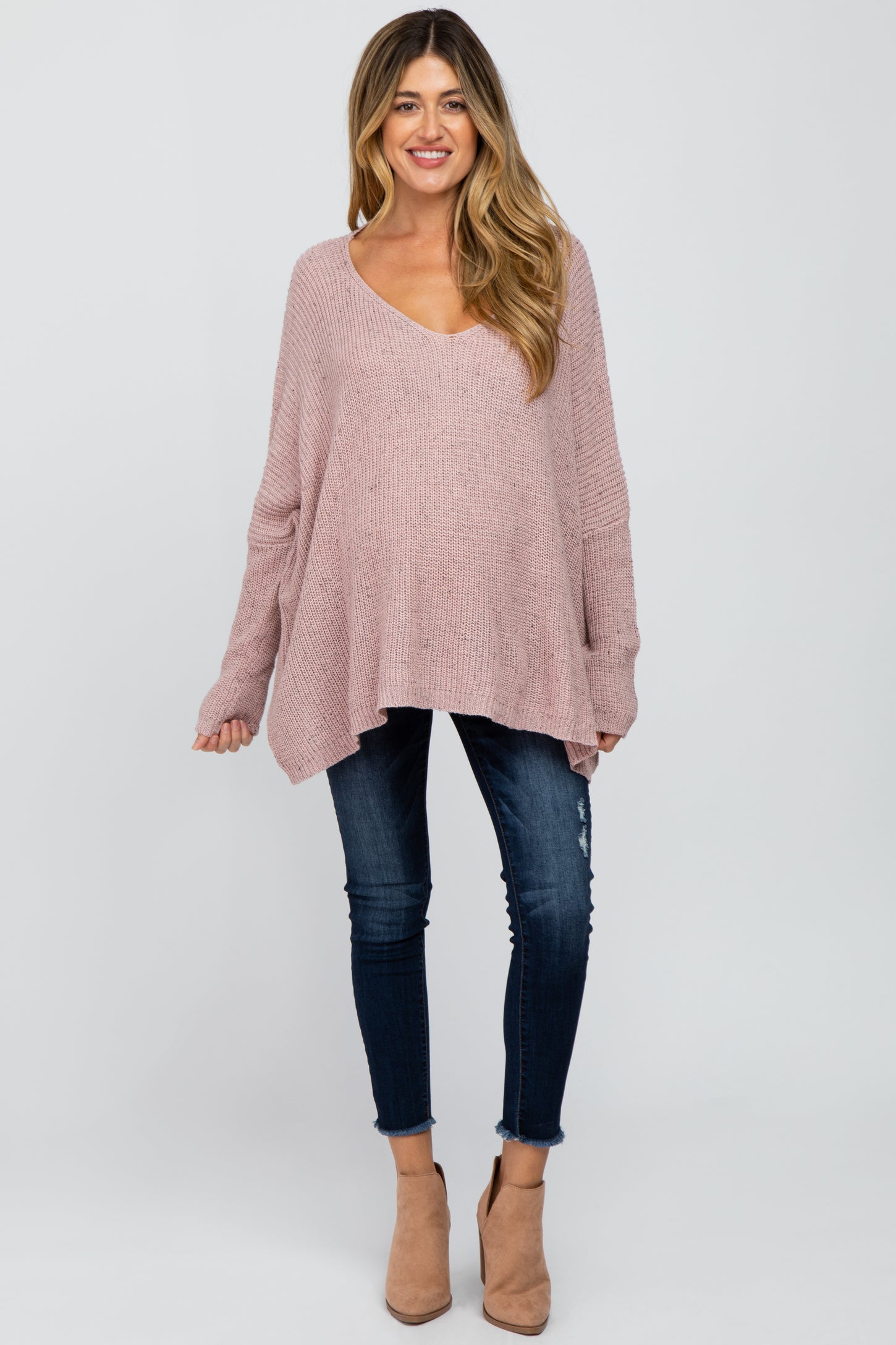 woman wearing a dusty rose oversized maternity sweater with a v-neck and distressed skinny jeans, showing her baby bump