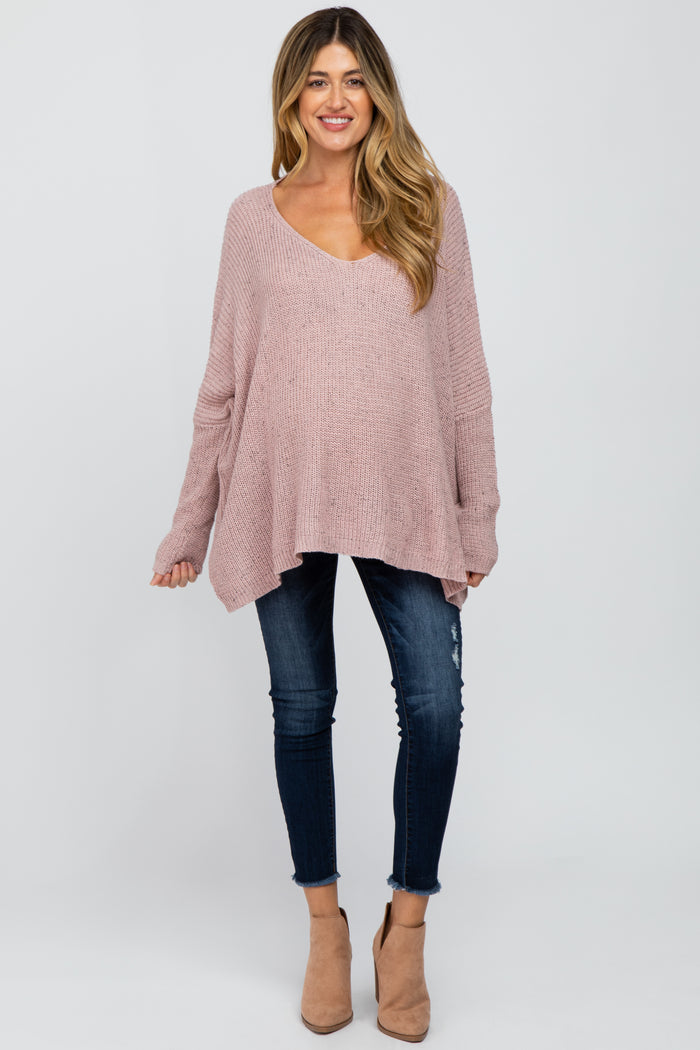 woman wearing a dusty rose oversized maternity sweater with a v-neck and distressed skinny jeans, showing her baby bump