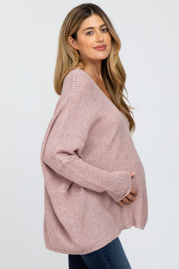 woman wearing a blush pink oversized maternity sweater and cradling her baby bump