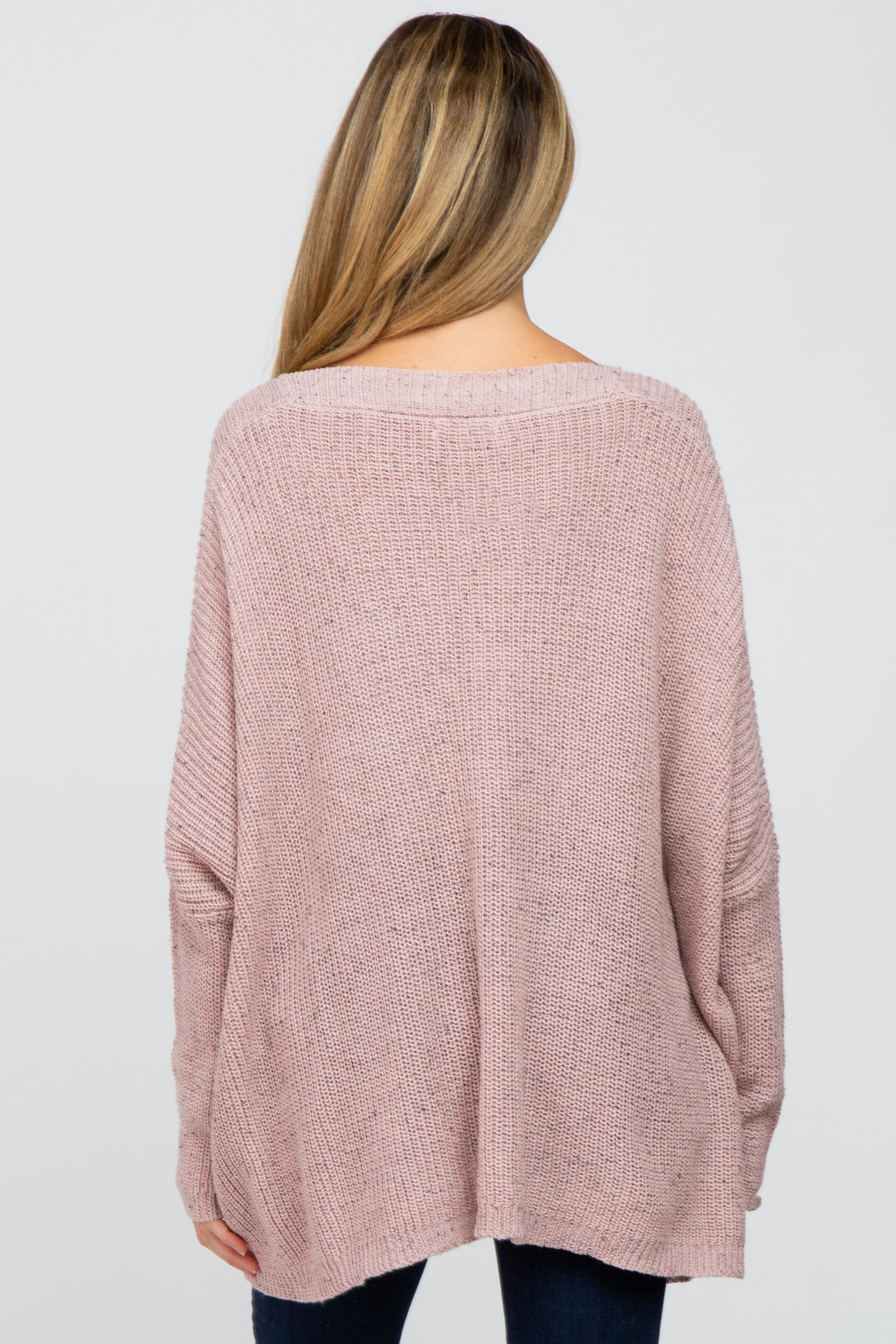 woman wearing a loose-fitting pale pink maternity sweater, seen from the back