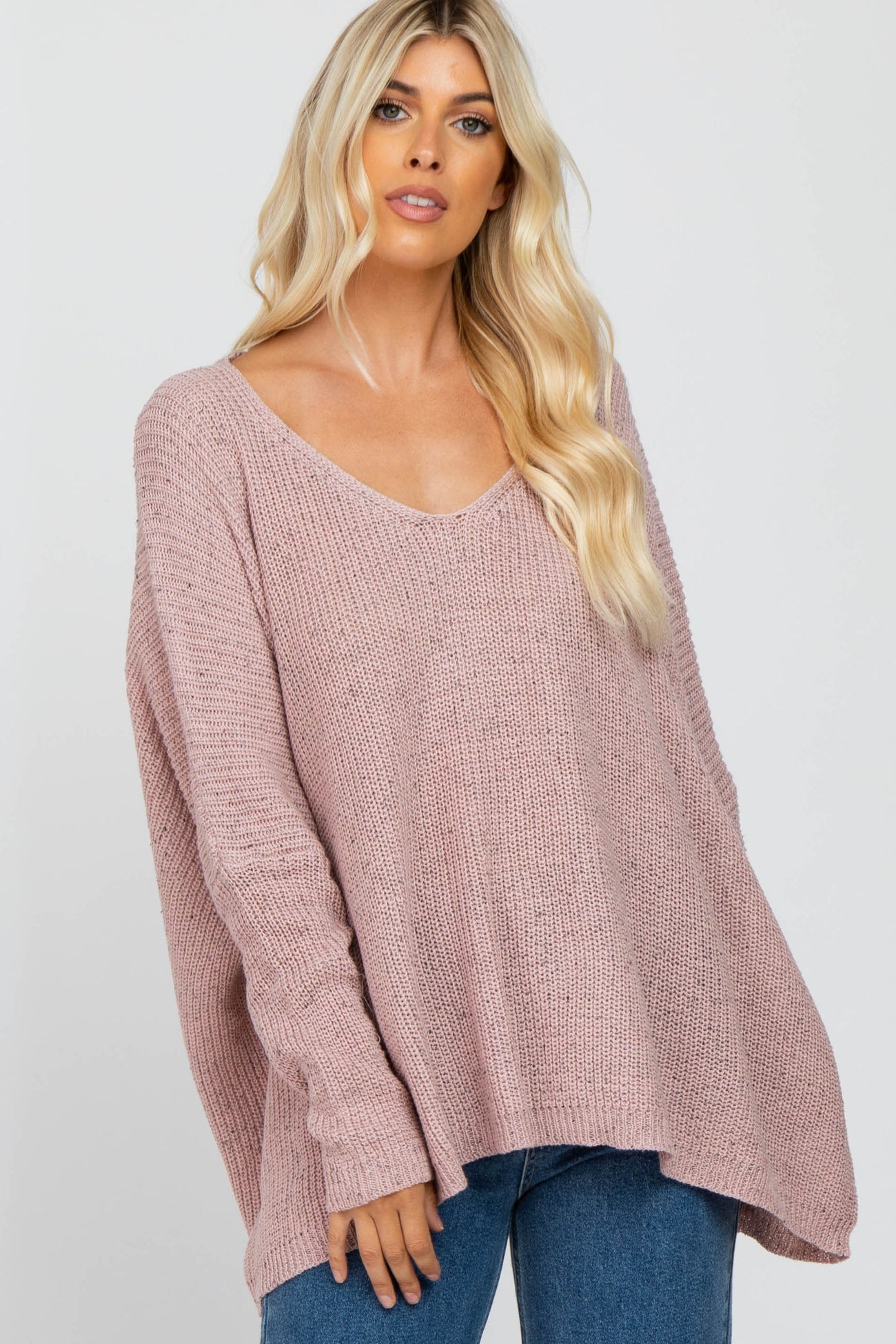 Woman wearing an oversized mauve V-neck knit sweater and blue jeans against a white background