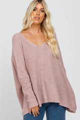 Woman wearing an oversized mauve V-neck knit sweater and blue jeans against a white background