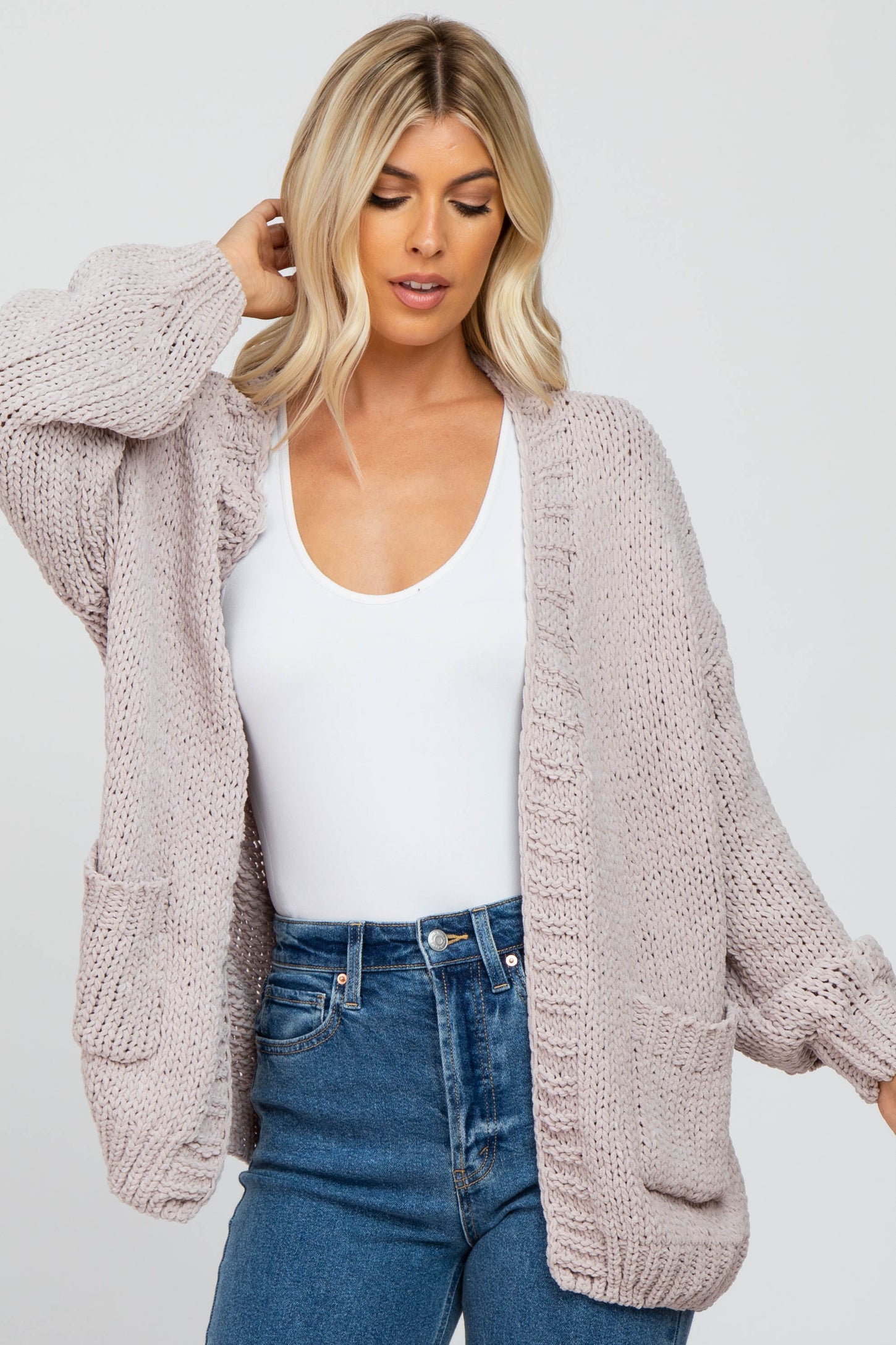 woman wearing a light pink oversized knitted cardigan with pockets over a white top and high-waisted denim jeans