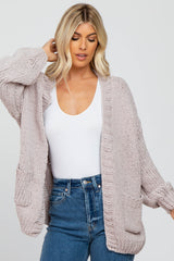 woman wearing a light pink oversized knitted cardigan with pockets over a white top and high-waisted denim jeans