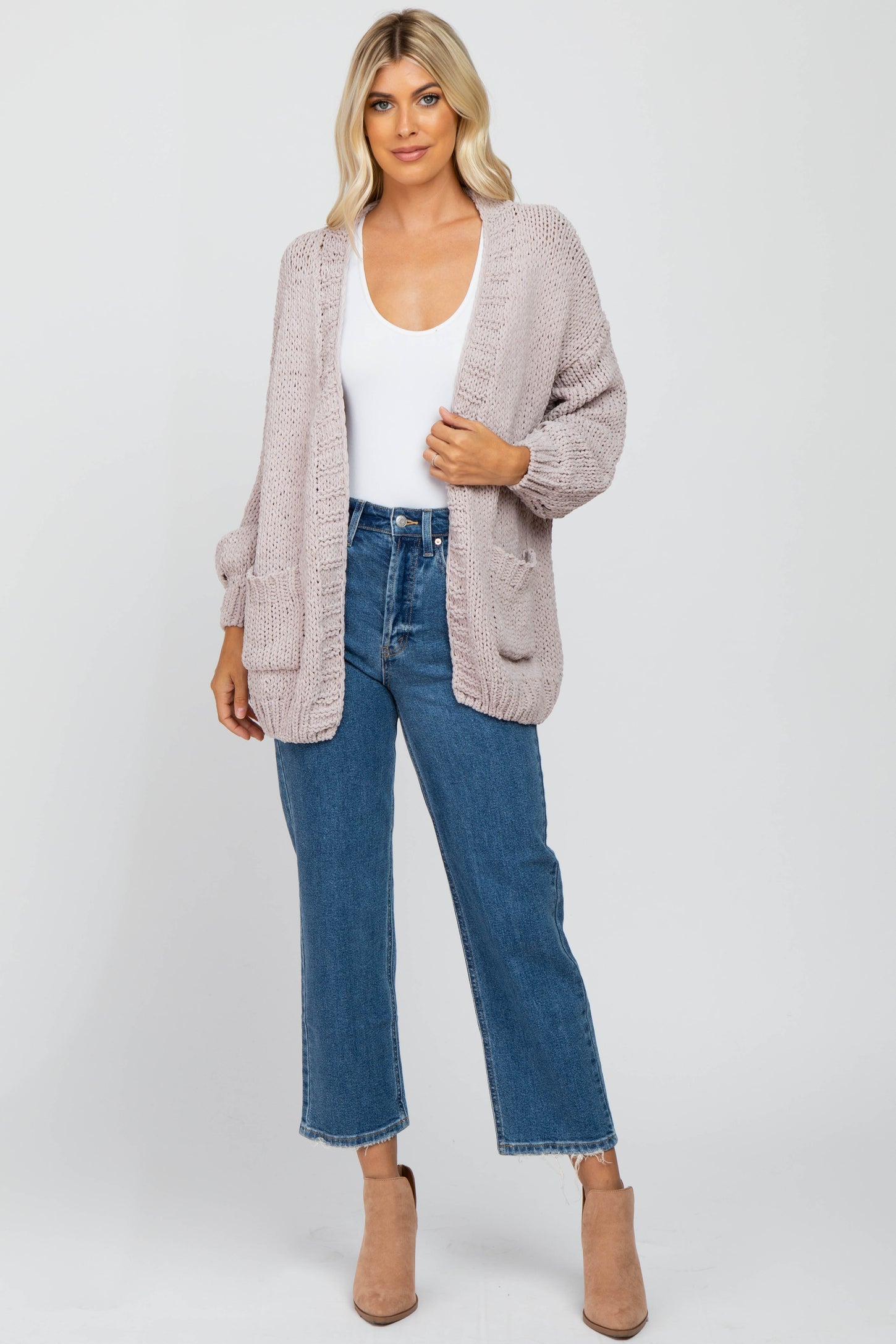 woman wearing a light mauve open knit cardigan over a white tank top and blue high-waisted jeans