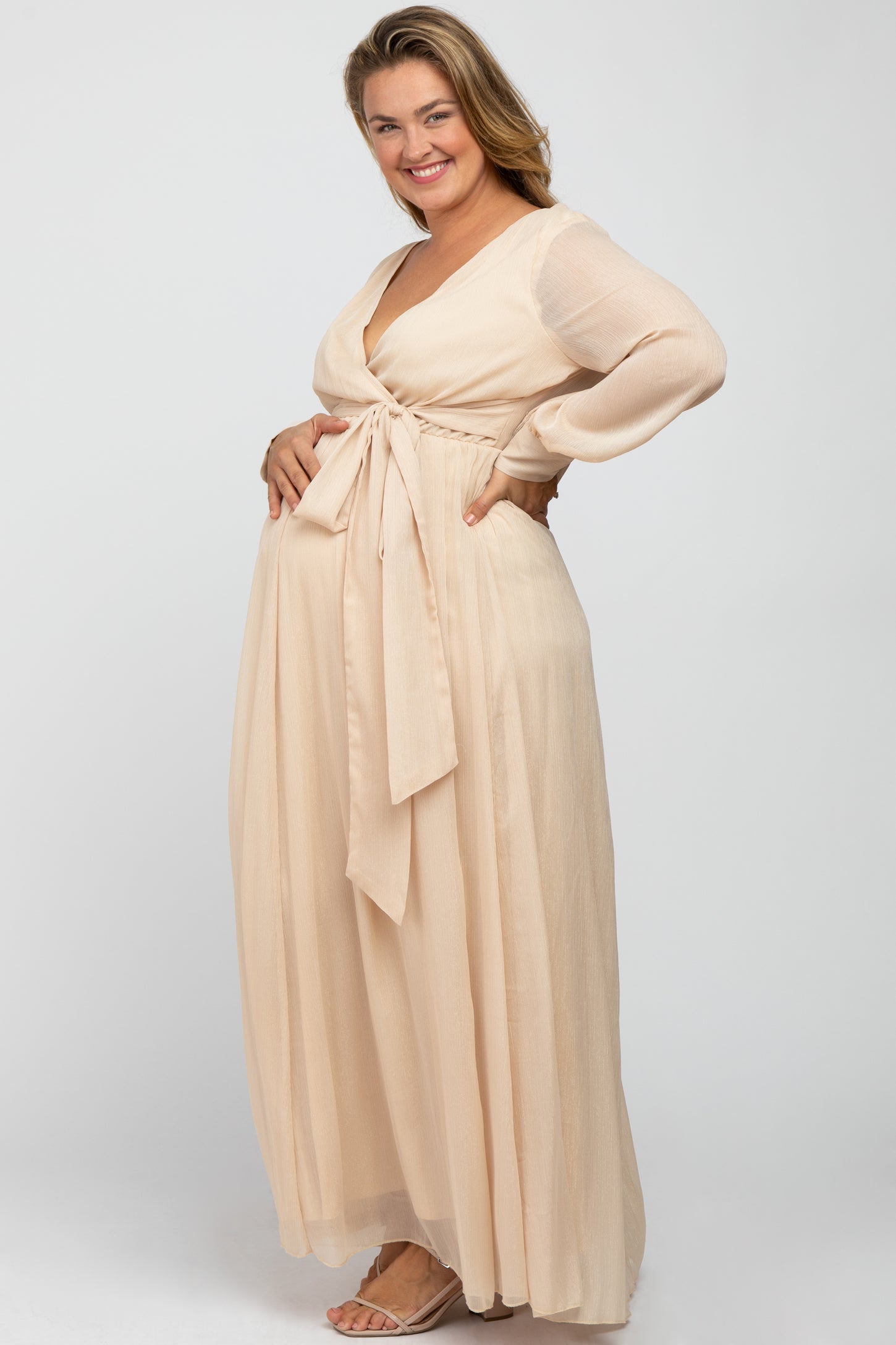 woman wearing a beige maternity plus wrap dress with long sleeves and a tied waist, showcasing her baby bump