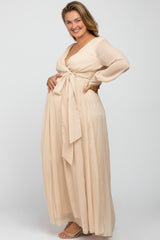 woman wearing a beige maternity plus wrap dress with long sleeves and a tied waist, showcasing her baby bump