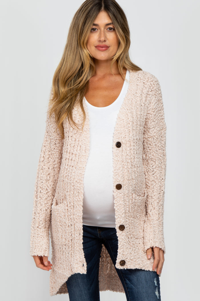 pregnant woman wearing a light pink popcorn knit maternity cardigan over a white top and blue jeans