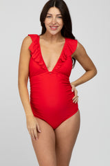 woman wearing a red ruffled maternity swimsuit, posing with a visible baby bump