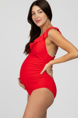 woman wearing a red maternity swimsuit with ruffle details and holding her baby bump