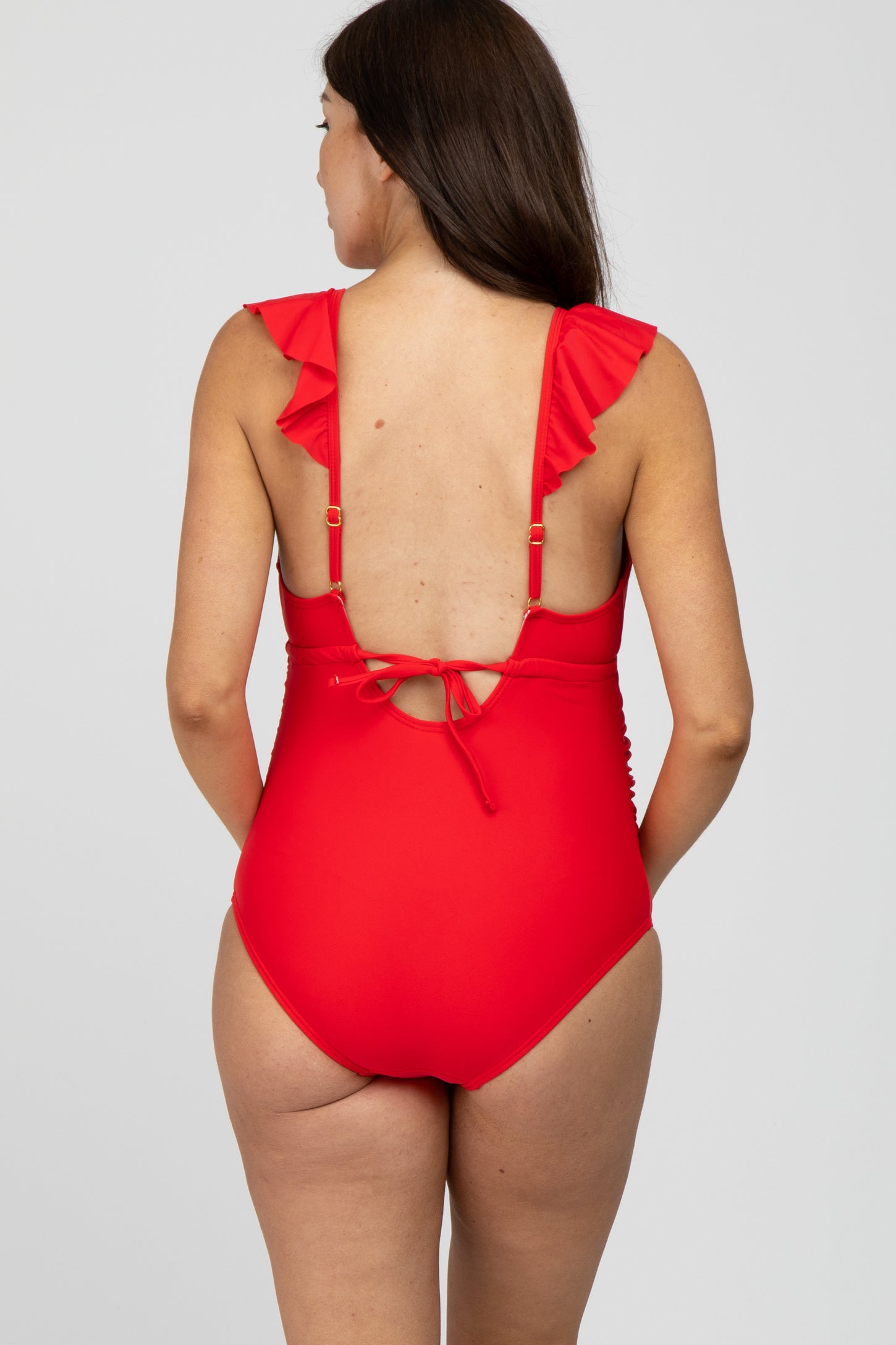 woman wearing a red maternity swimsuit with ruffle straps and a tie back detail, showing a baby bump
