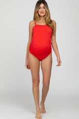 woman wearing a red maternity swimsuit with adjustable straps and a ruched side design, showcasing her baby bump