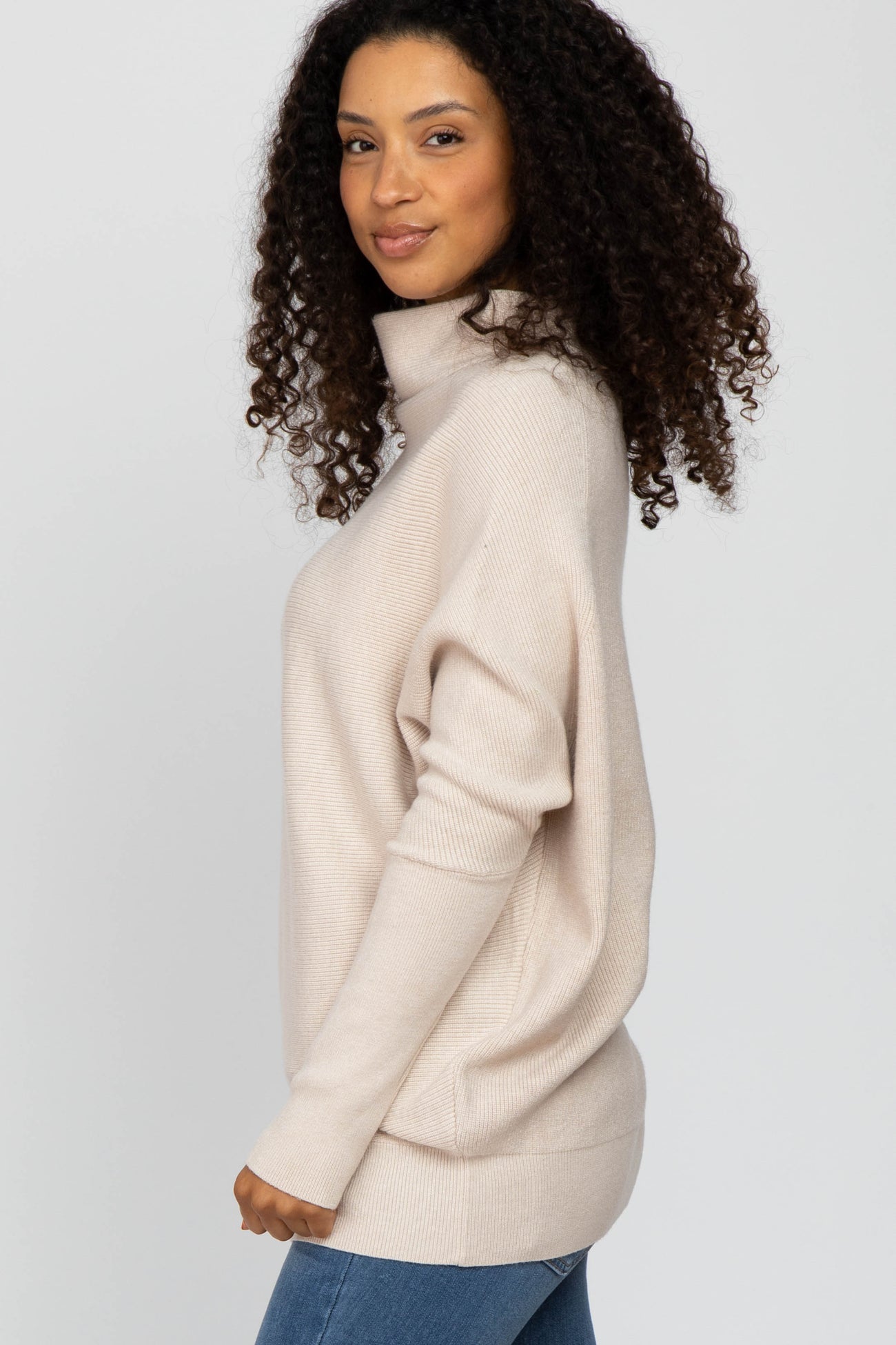 woman wearing a light beige turtleneck sweater with a relaxed fit and side slits, standing sideways