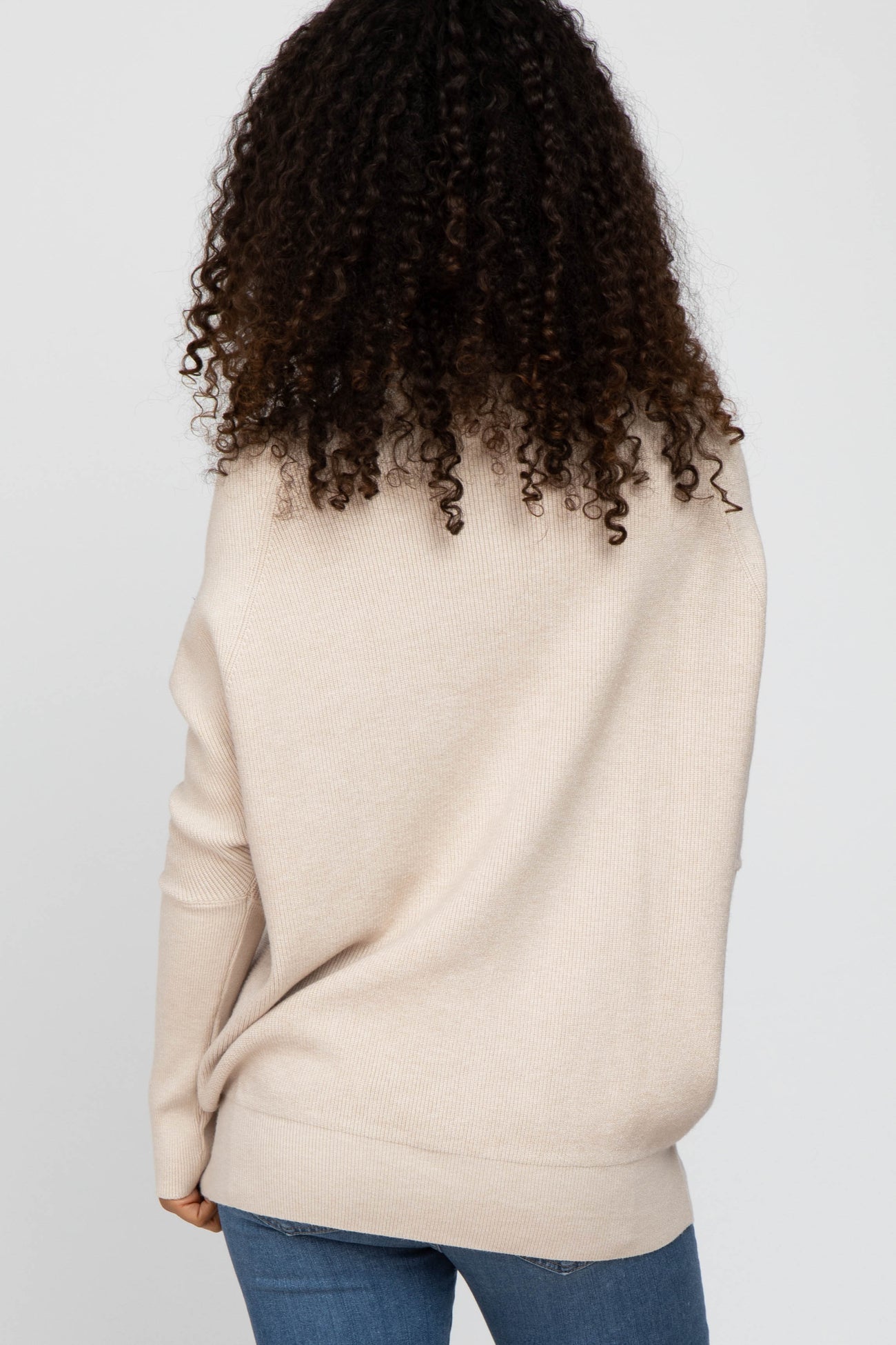 woman wearing a beige oversized sweater with a relaxed fit and long sleeves, styled with blue jeans