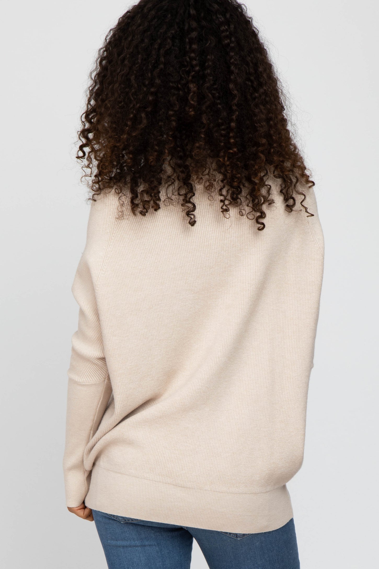 woman wearing a beige oversized sweater with a relaxed fit and long sleeves, styled with blue jeans