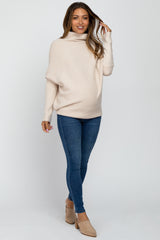 woman wearing a light beige maternity sweater with a draped neckline and blue skinny jeans, showing her baby bump