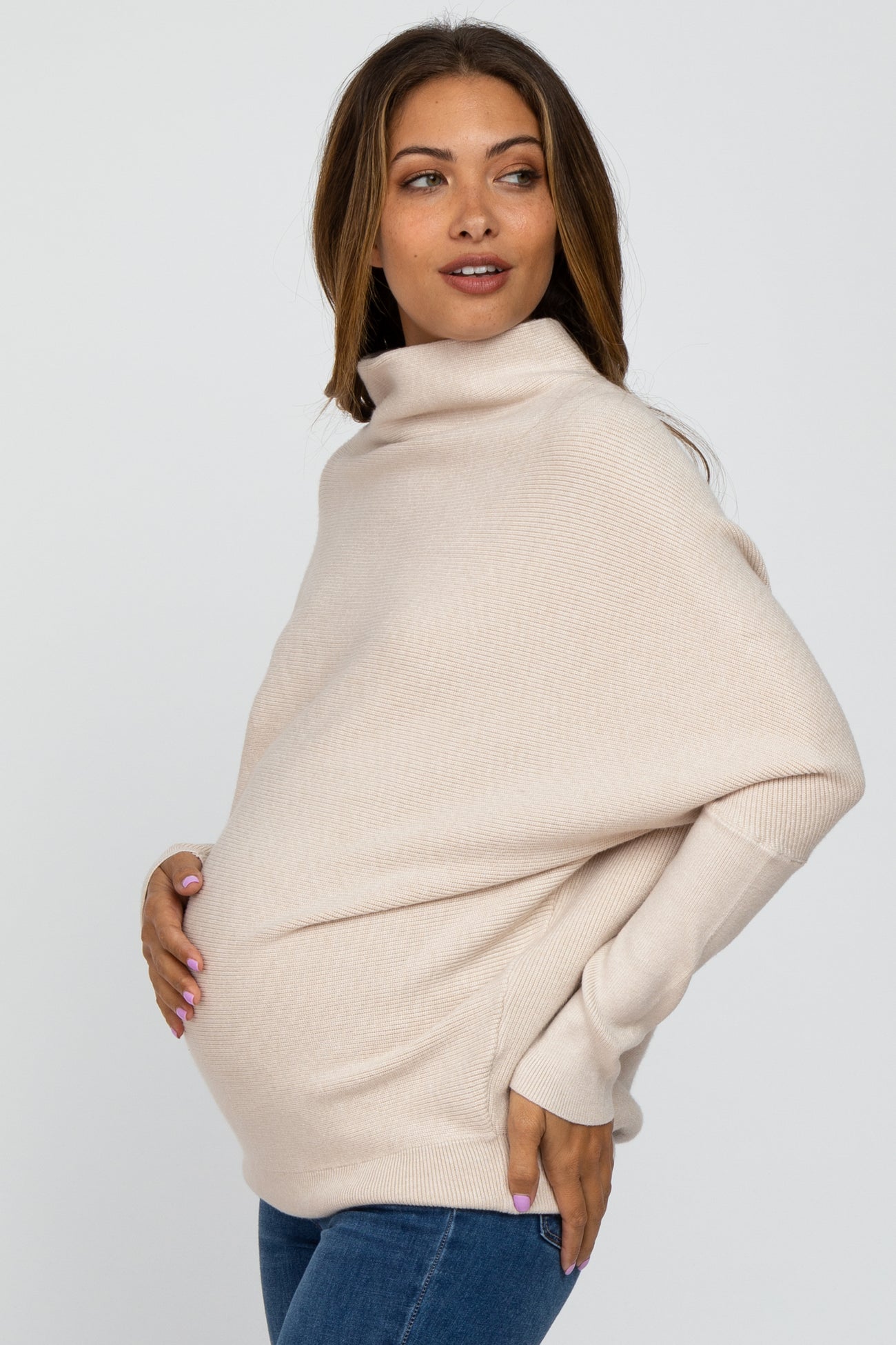 woman wearing a beige oversized maternity sweater and showing her baby bump
