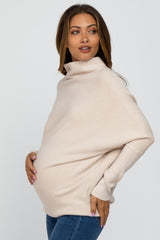 woman wearing a beige oversized maternity sweater and showing her baby bump