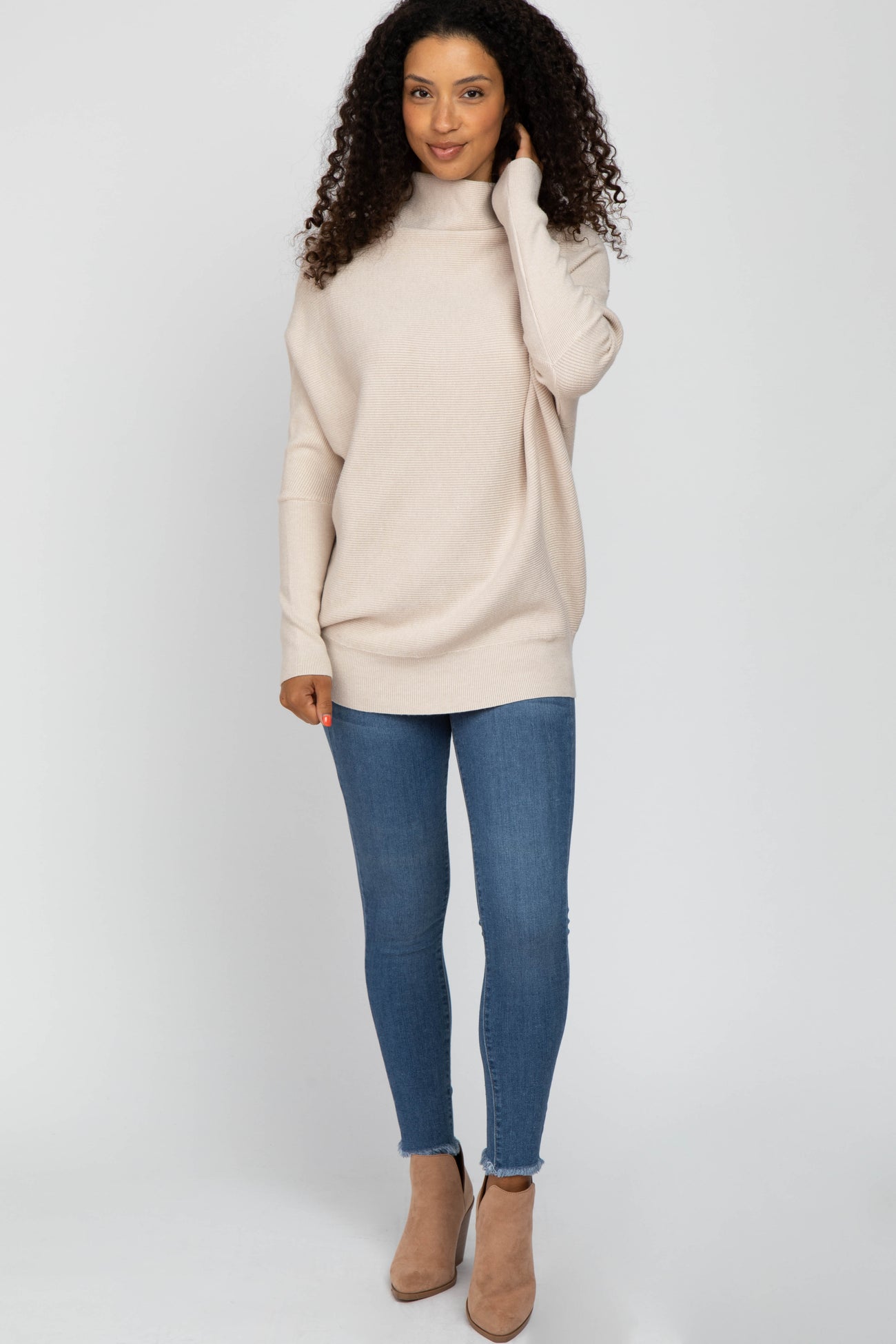 woman wearing a light beige oversized sweater with a turtleneck, paired with blue skinny jeans and beige heeled booties