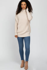 woman wearing a light beige oversized sweater with a turtleneck, paired with blue skinny jeans and beige heeled booties
