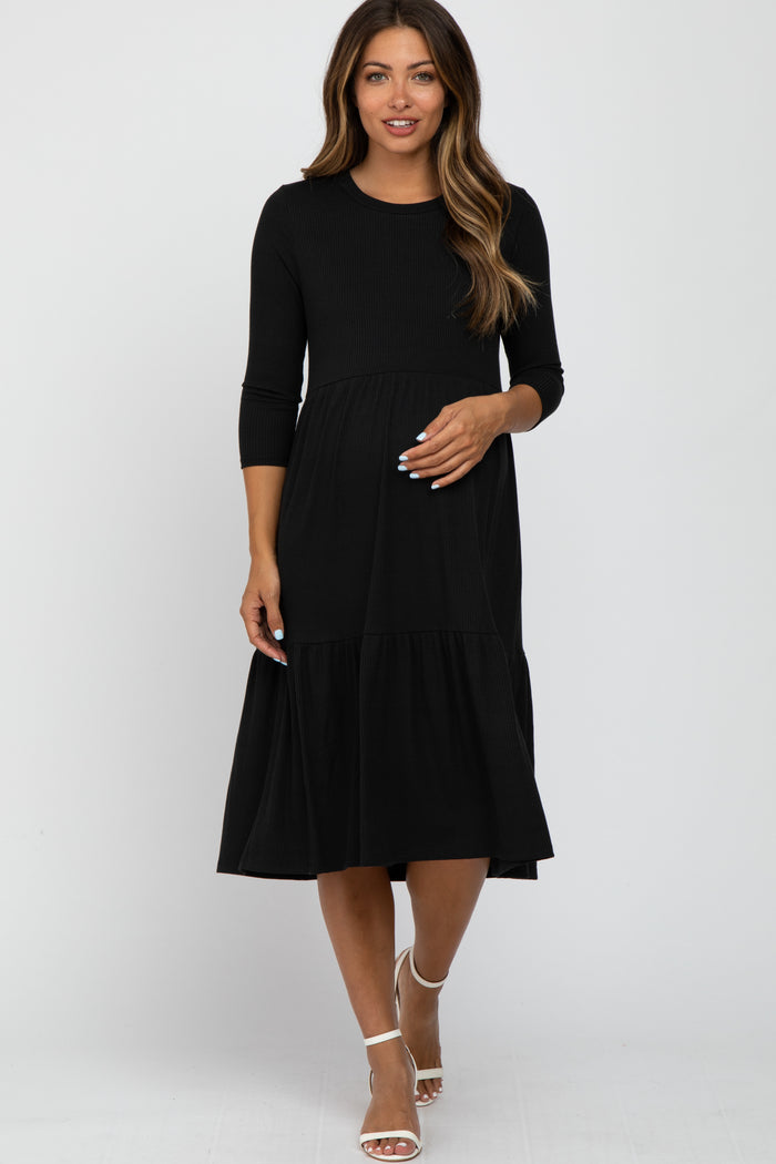 woman wearing a black ribbed long sleeve tiered maternity midi dress with white heels