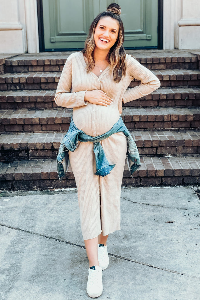 smiling pregnant woman in beige ribbed maternity dress and denim jacket standing on stone steps