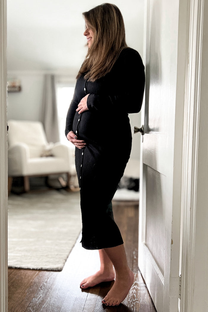 pregnant woman in black ribbed midi dress holding her baby bump while standing in a doorway