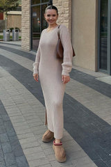 woman wearing a beige ribbed knit maxi dress with side slits and brown slip-on shoes, holding a brown handbag