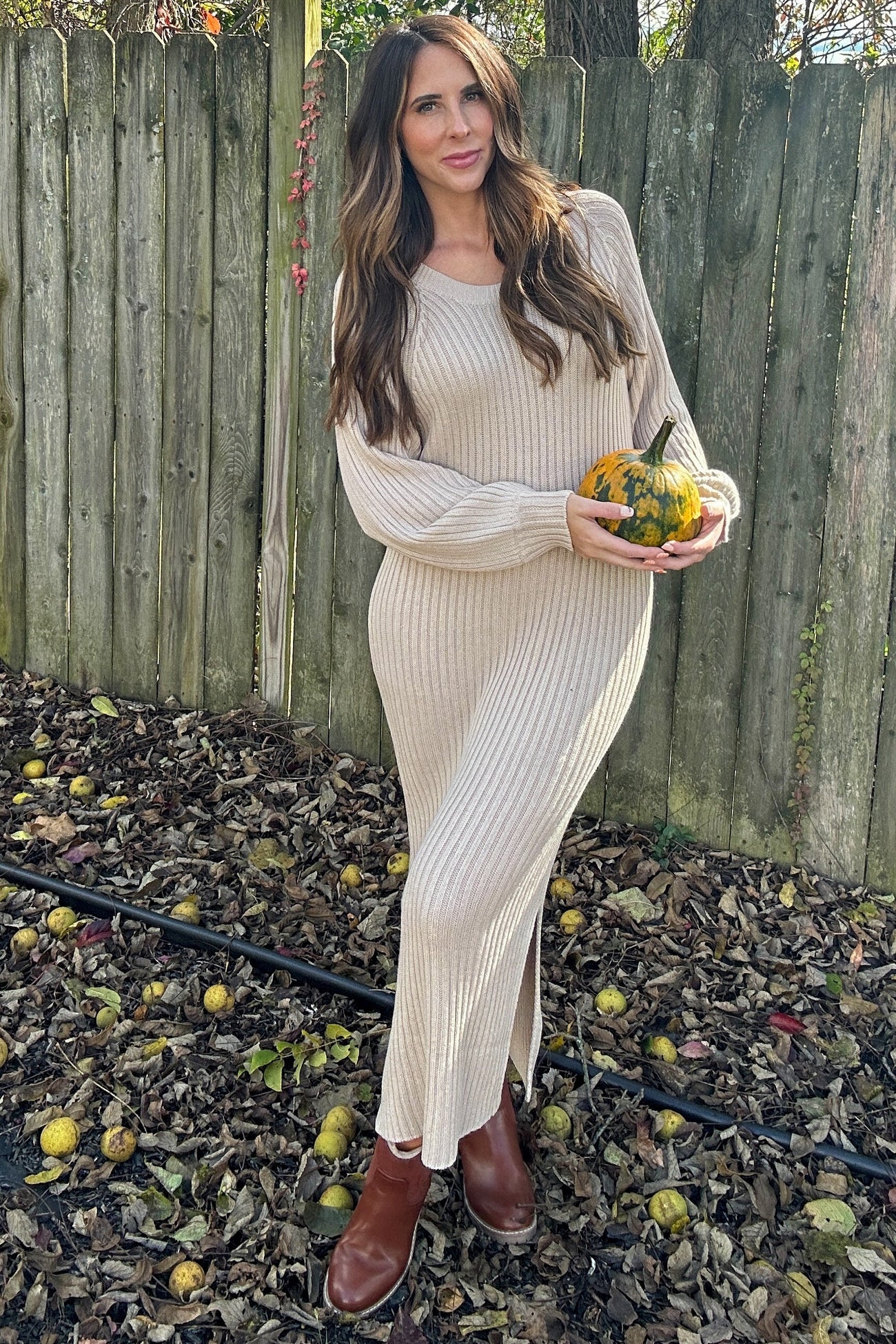 woman wearing a beige ribbed knit maxi dress and holding a small pumpkin in an outdoor setting