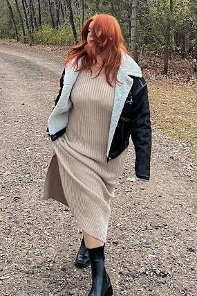 woman wearing a beige ribbed midi dress and a black denim jacket walking on a gravel path in a forested area