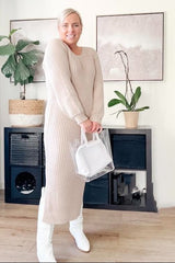 woman wearing a beige ribbed long sleeve sweater dress and holding a clear handbag, standing in a bright indoor setting