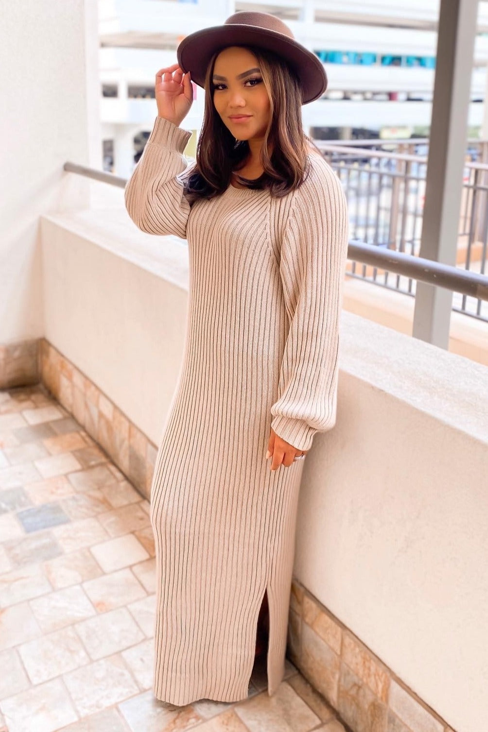 woman wearing a beige ribbed knit maxi dress with long sleeves and side slits, accessorized with a wide-brim hat