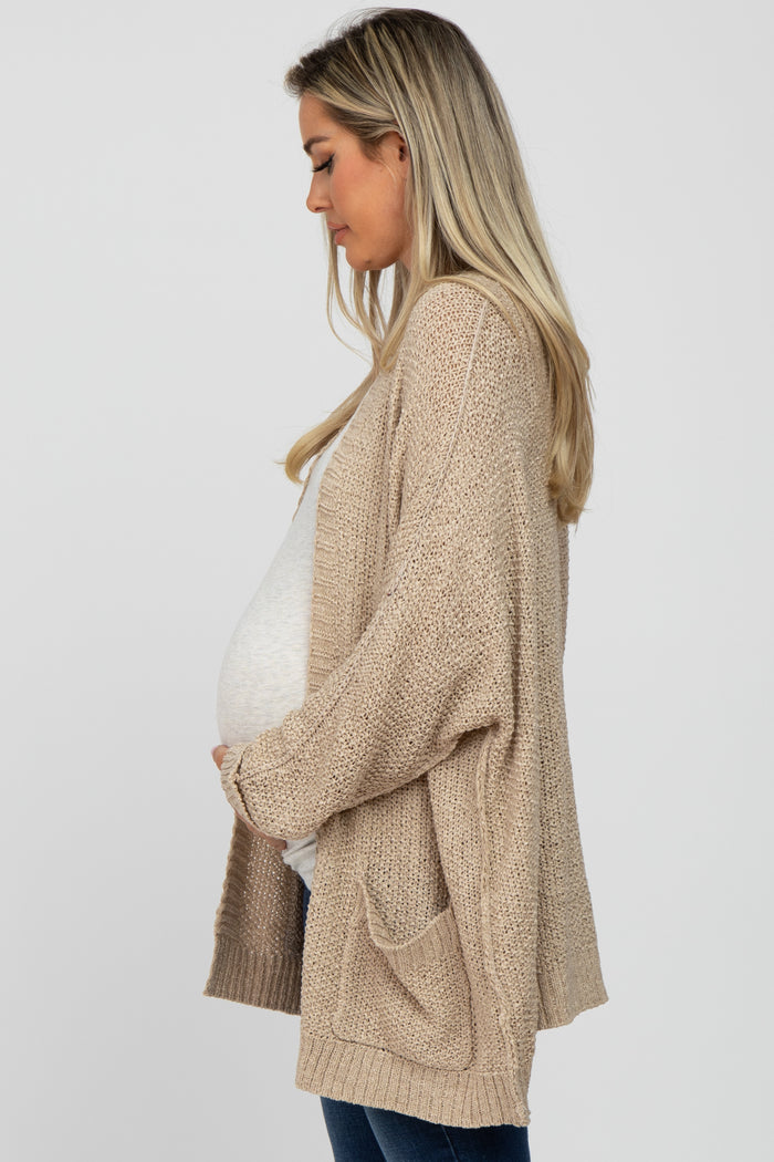 woman wearing a light beige open-knit maternity cardigan and holding her baby bump